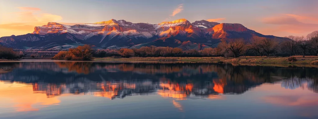 a majestic mountain landscape at sunrise, with vibrant orange and pink hues illuminating the peaks against a crystal-clear sky, reflecting in a serene, glassy lake below.