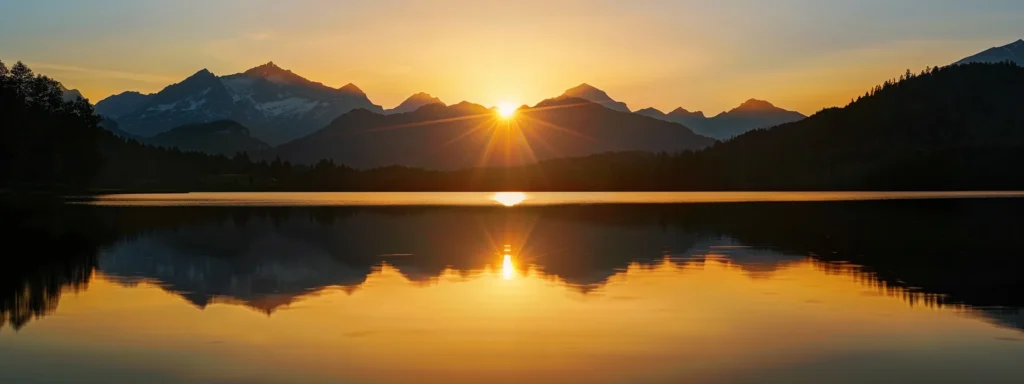 a vibrant sunset casts golden hues over a tranquil lake, reflecting the magnificent silhouettes of towering mountains under a clear sky.